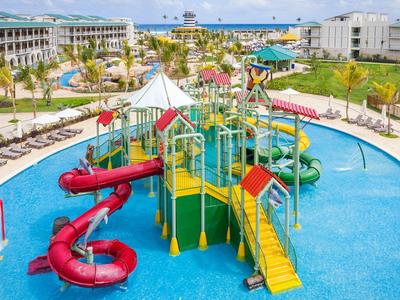 Bunter Wasserspielplatz mit Rutschen in einem Resort mit Hotelgebäuden im Hintergrund.