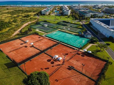 Vogelperspektive auf Tennisplätze neben Hotelgebäuden nahe Küste und Dorf.