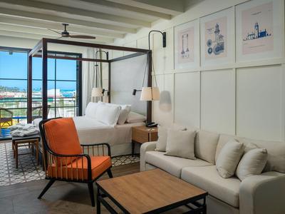 Modernes Hotelzimmer mit Meerblick, Terrasse, Bett, Sofa und orangefarbenem Sessel.