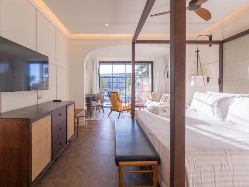 Modernes Schlafzimmer mit großem Bett, Holzmöbeln und Blick auf eine Terrasse bei Tageslicht.