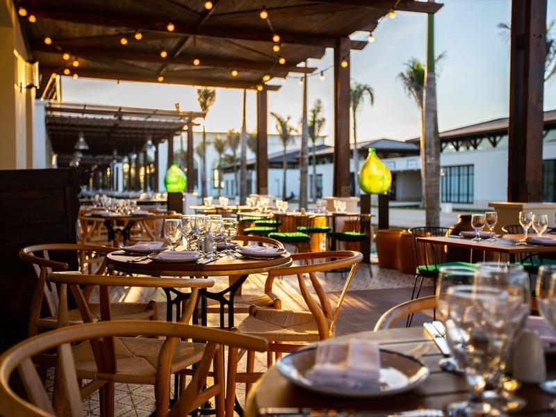 Terrassenrestaurant bei Sonnenuntergang mit Holztischen, Stühlen und warmen Lichterketten.