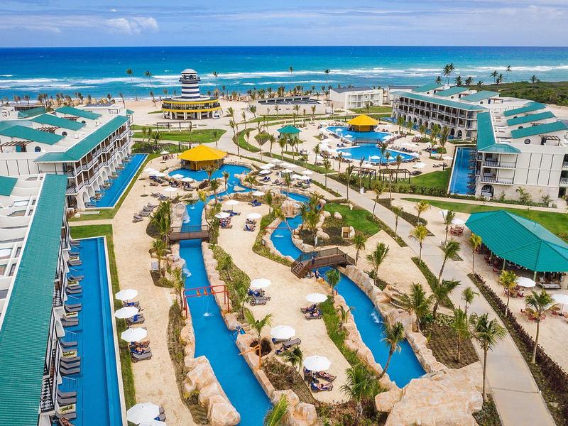 Großes Resort mit mehreren Gebäuden, Poollandschaft, Palmen und Blick auf das blaue Meer.