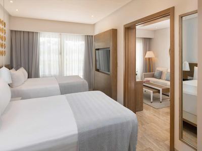 Modernes Hotelzimmer mit zwei Doppelbetten, Holzakzenten und angrenzendem Wohnzimmer.