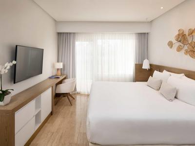 Helles modernes Schlafzimmer mit großem Bett, Holzdetails, Teppich und großem Fenster mit Vorhängen.