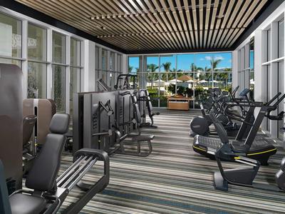 Gimnasio moderno con varios aparatos de ejercicio y gran ventana con vista al área exterior.