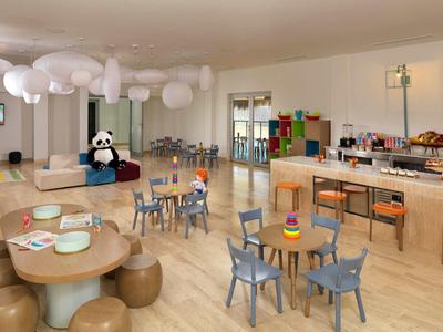 Kinderfreundlicher Speiseraum mit bunten Stühlen, runden Tischen und Panda-Plüsch als Dekor.