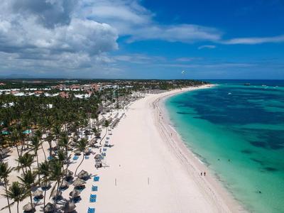 Langer weißer Sandstrand mit Palmen, türkisblauem Meer und blauem Himmel mit Wolken.