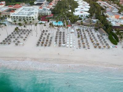 Strand mit Reihen von Liegestühlen und Sonnenschirmen vor Hotelanlagen und grüner Vegetation.