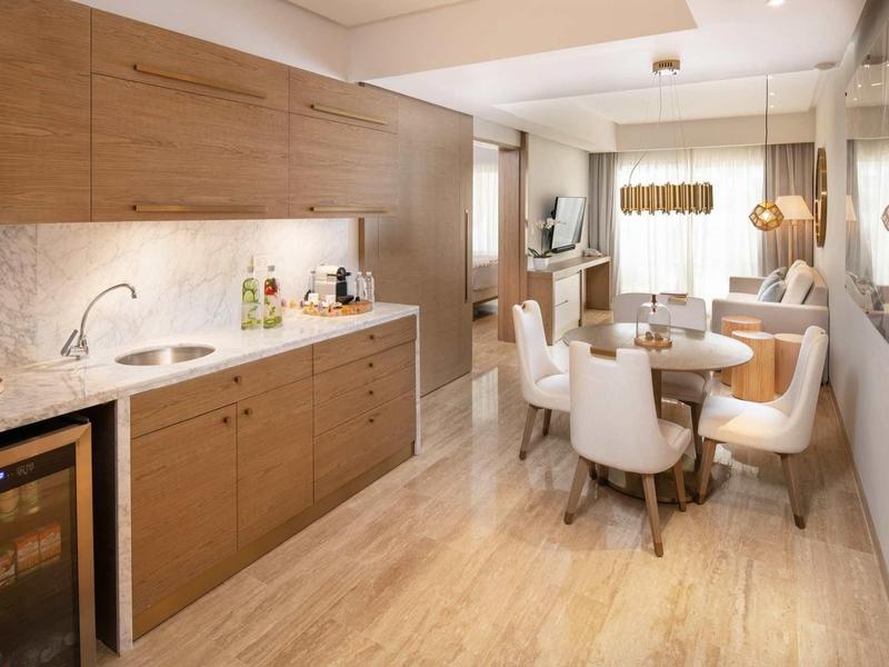 Moderne Küche mit Holzschränken, hellem Boden, rundem Esstisch und weiß gepolsterten Stühlen.