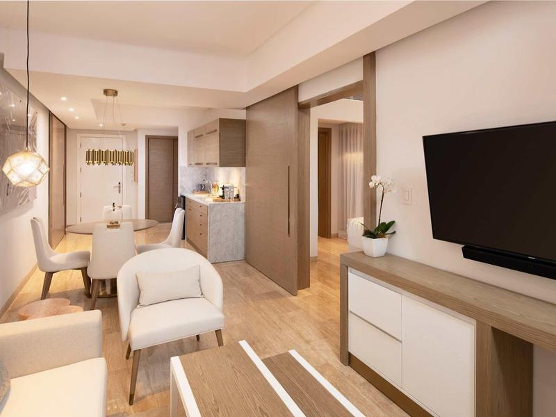 Moderner Wohnraum mit hellem Holzfußboden, weißen Möbeln, Fernseher und Esstisch am Fenster.