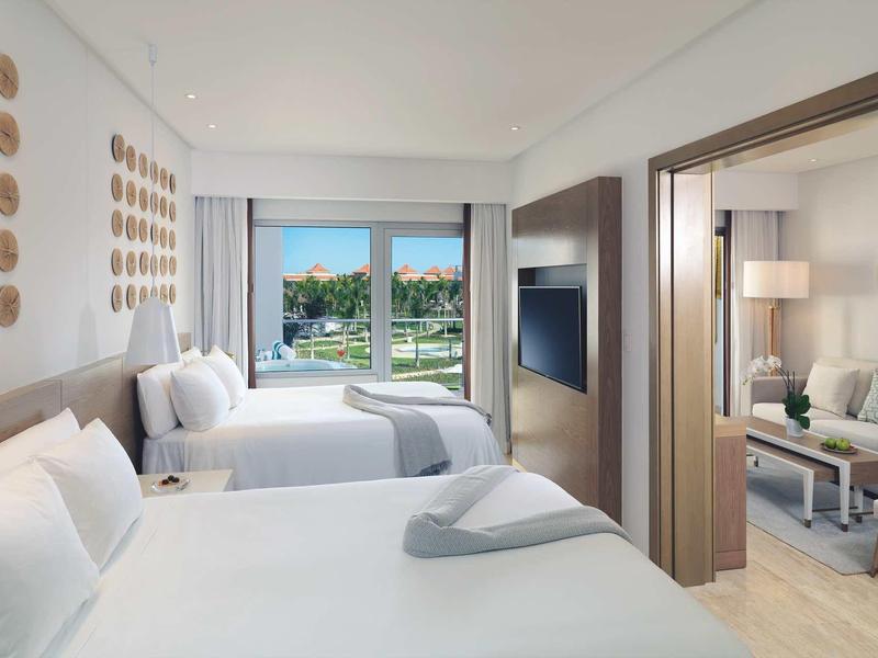 Hotelzimmer mit zwei Doppelbetten, modernem Design, TV und Blick auf eine grüne Landschaft durch das Fenster.