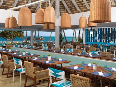 Ristorante luminoso e aperto con mobili in legno e vista sul mare sotto un soffitto bianco alto.