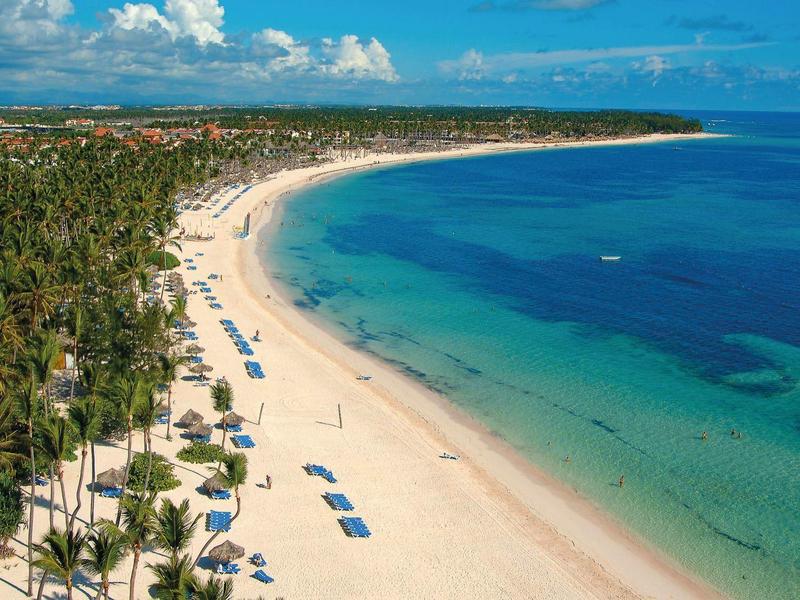 Vista di una larga spiaggia sabbiosa tropicale con palme e mare blu.
