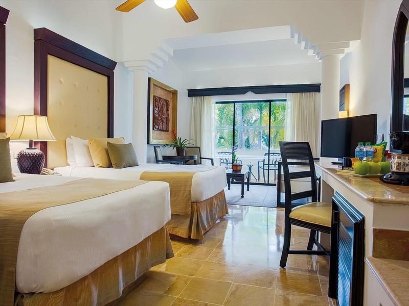 Camera d'hotel con due letti, scrivania, TV e balcone con vista sul giardino