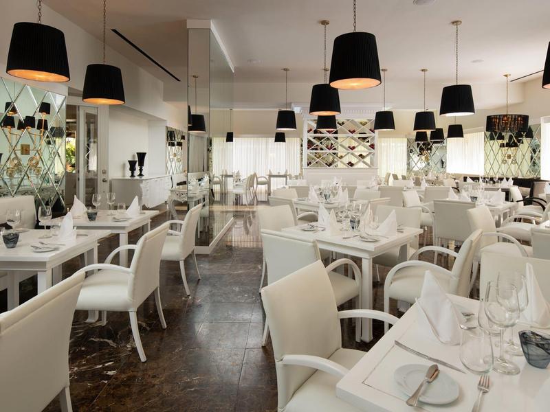 Ristorante elegante con sedie bianche, tavoli apparecchiati e lampade a sospensione nere.