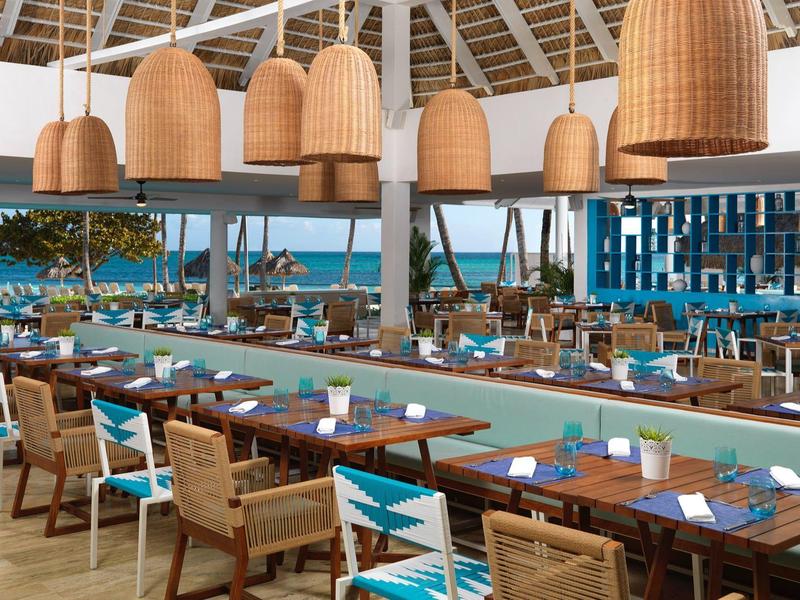 Ristorante luminoso e aperto con mobili in legno e vista sul mare sotto un soffitto bianco alto.