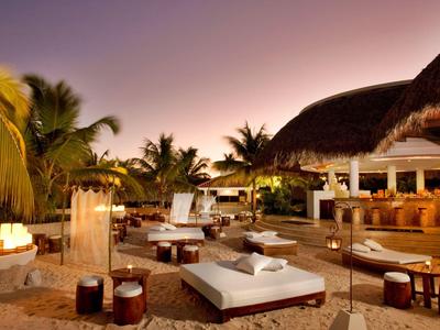 Lounge di lusso sulla spiaggia con lettini, candele e palme al tramonto.