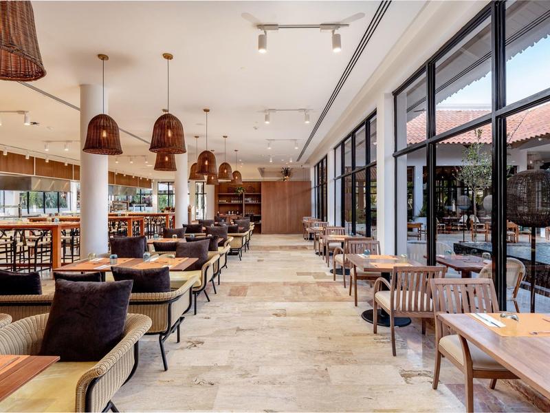 Moderní restaurace s dřevěnými stoly, křesly a velkými okny na terasu.