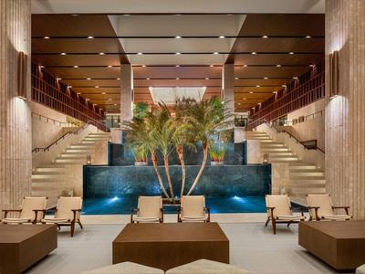 Großer Hotel-Lobbybereich mit Palmendekoration, Treppen und Sitzgelegenheiten entlang eines Wasserelements.