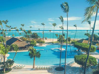 Velká oblast bazénu s palmami a výhledem na moře pod jasnou oblohou.