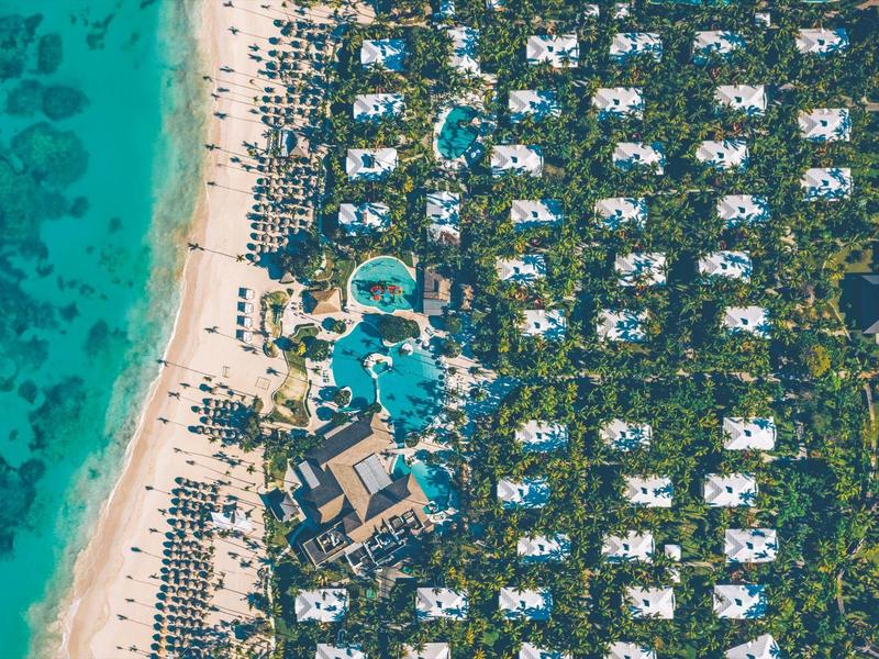 Letecký pohled na resort s bazénem, řadami bungalovů a pláží s modrým mořem.