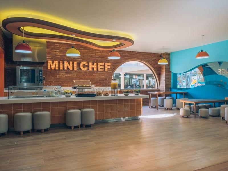 Moderní, světlá mini kuchyňka v hotelu s barovými židličkami a sedacími místy.