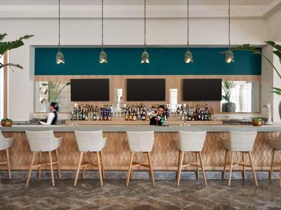 Espace bar d'hôtel moderne avec tabourets blancs, comptoir en bois et mur vert en arrière-plan.