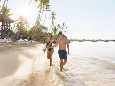 Couple marchant sur une plage ensoleillée avec des palmiers et de l'eau claire.