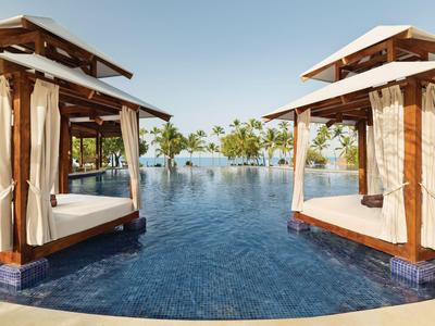 Deux lits de piscine luxueux avec rideaux au bord d'une piscine à débordement avec vue sur des palmiers.