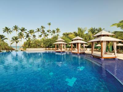 Grande piscine avec pavillons et palmiers sous un ciel dégagé dans une station tropicale