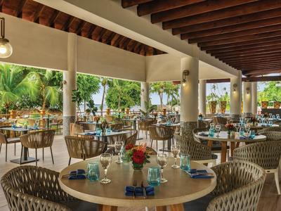 Espace restaurant d'hôtel ouvert avec tables, chaises et vue sur des plantes tropicales.