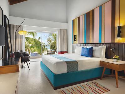 Chambre d'hôtel moderne avec grand lit, décoration murale colorée et vue sur la piscine et les palmiers