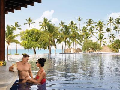 Couple se détend dans la piscine avec vue sur les palmiers et la mer par temps ensoleillé.