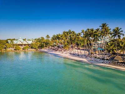 Agua turquesa en la playa tranquila con palmeras y sombrillas oscuras bajo un cielo despejado