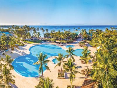 Großer Hotelpool mit Palmen und Blick aufs Meer an einem sonnigen Tag.