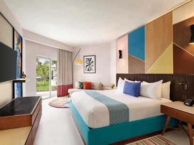 Habitación de hotel luminosa con cama grande, cabecero colorido y acceso al jardín.