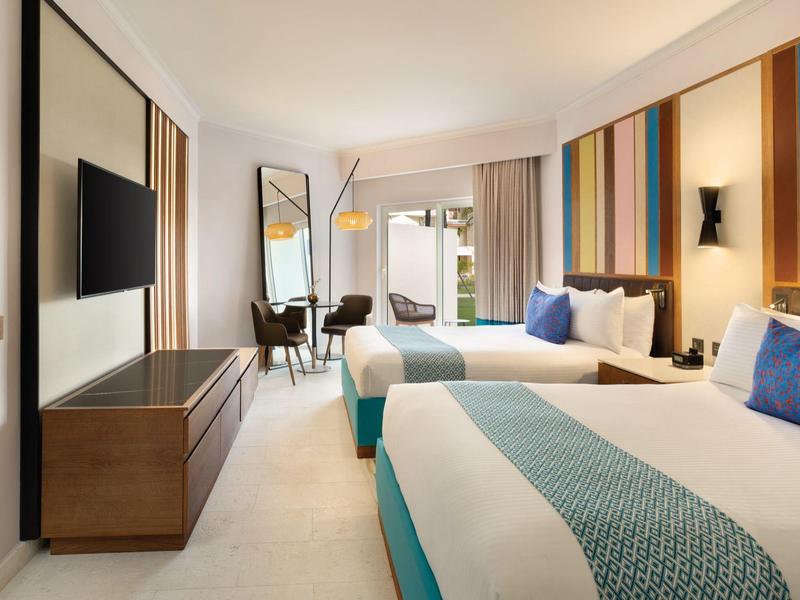 Habitación de hotel moderna con dos camas, TV, escritorio y acentos de pared coloridos.