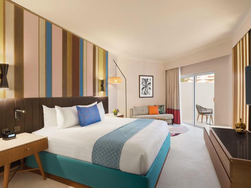 Habitación de hotel moderna con cama grande, pared a rayas, sofá y balcón con vista.