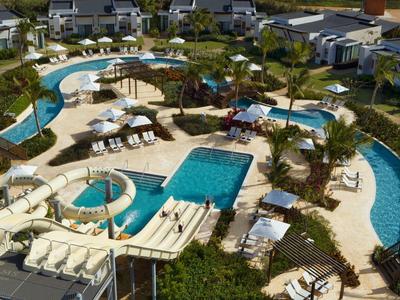 Gran área de piscina con toboganes, tumbonas y bungalows alrededor en un resort vacacional.