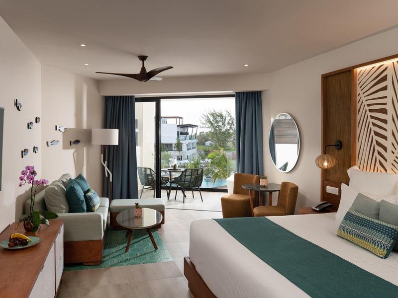 Habitación de hotel moderna con cama grande, área de descanso y vista a una terraza con jardín.