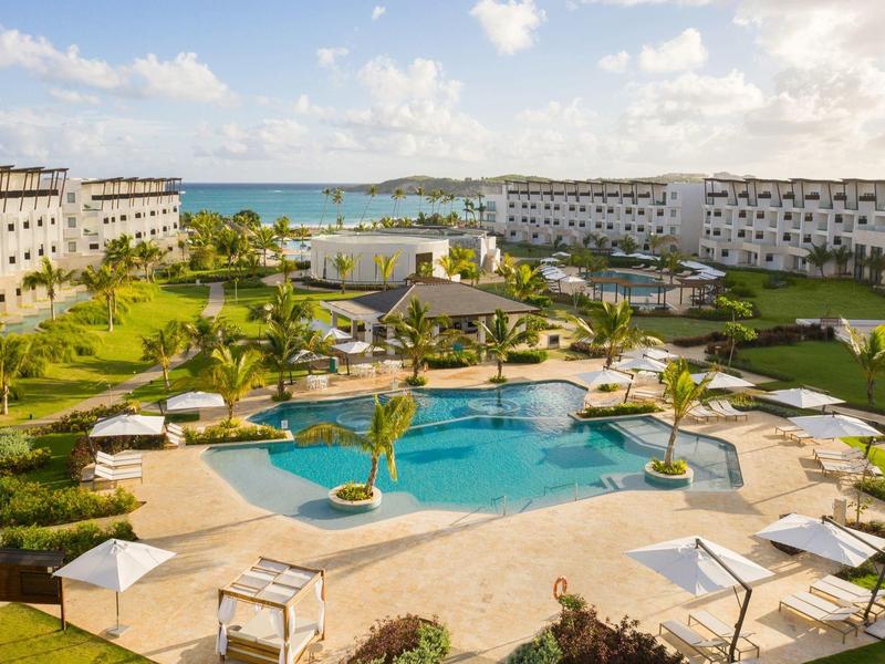Complejo hotelero con gran piscina, sombrillas y vista al mar bajo un cielo despejado.