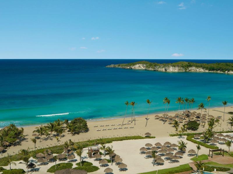 Playa con palmeras, sombrillas y agua azul clara bajo un cielo azul