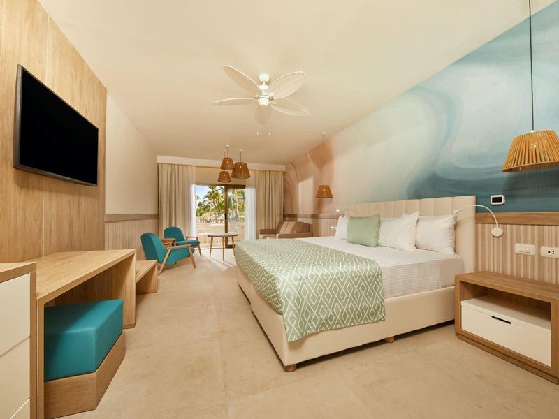 Modern hotel room with double bed, desk, chairs, and balcony with sea view.