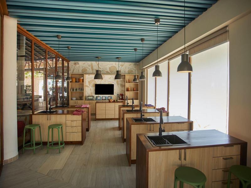 Modern restaurant with wooden furniture, green stools, and blue ceiling beams.