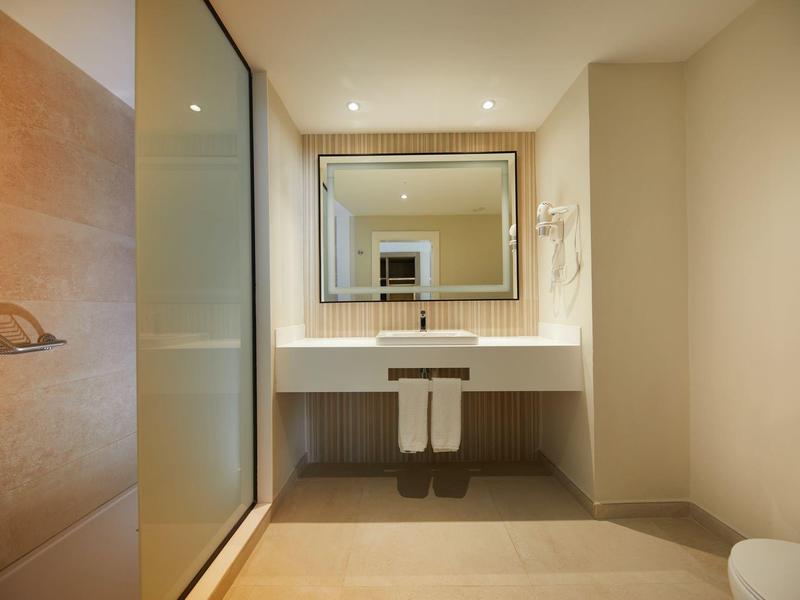 Modern hotel bathroom with large mirror, sink, and glass shower.