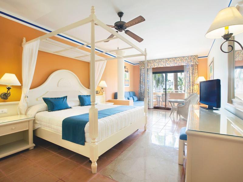 Bright hotel room with canopy bed, ceiling fan, and balcony access with a view.