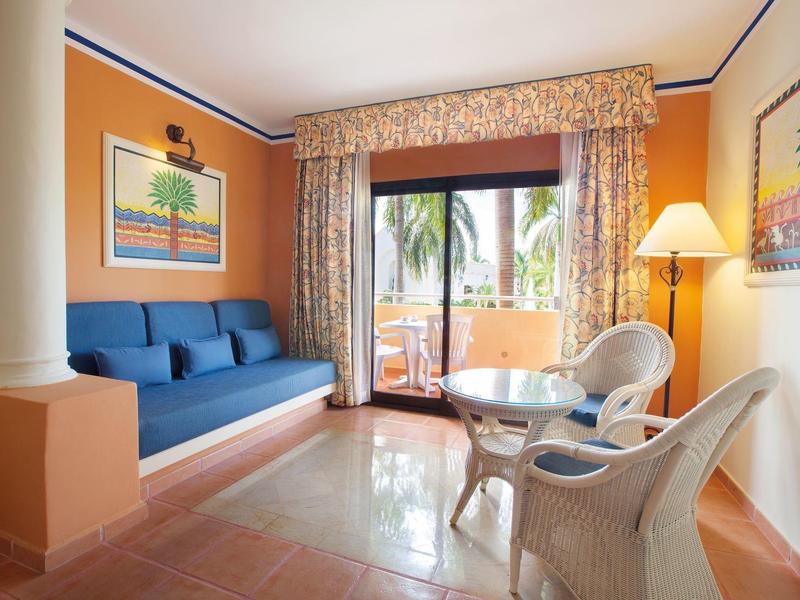 Bright living room with blue sofa, white chairs, and balcony view with palm trees.