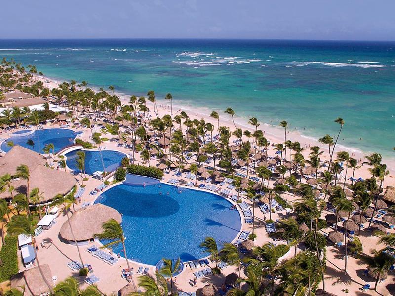 Hotel resort with large pools, palm trees, and direct access to the beach by turquoise sea.