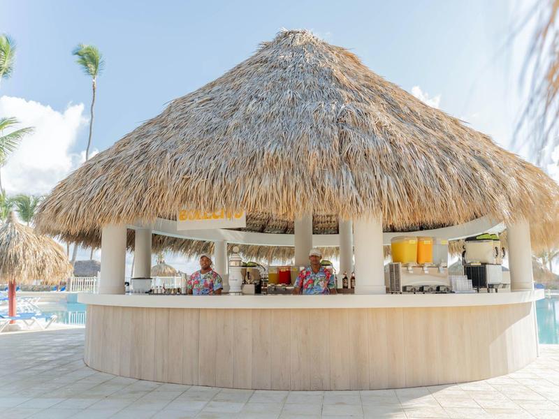 Thatched roof bar by pool at tropical resort on sunny day.