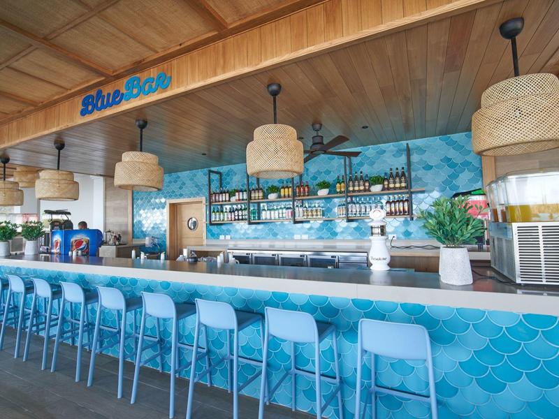 Modern beach bar with blue counter, bar stools, and wall featuring ocean mural.